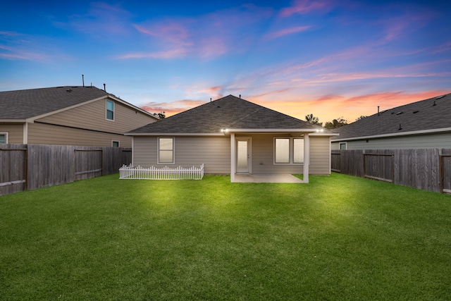 back house at dusk with a patio and a lawn