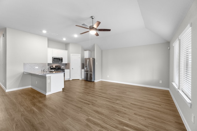 kitchen with stainless steel appliances, kitchen peninsula, white cabinets, dark wood-type flooring, and vaulted ceiling