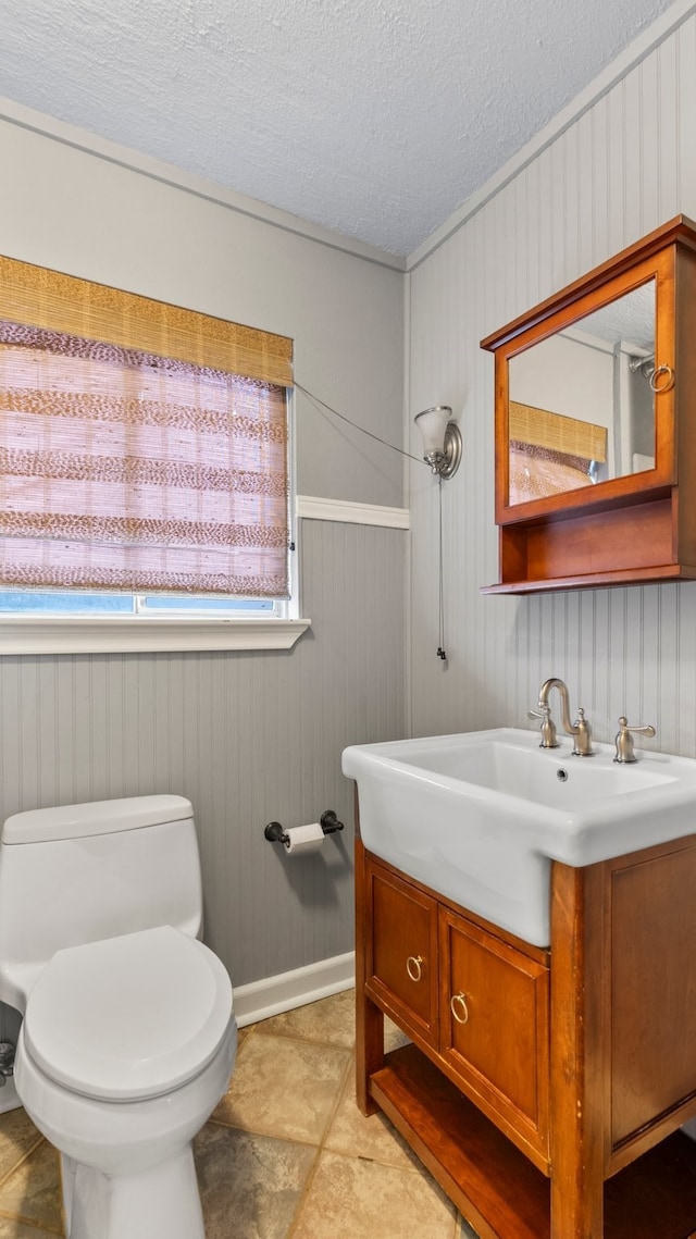 bathroom with a textured ceiling, vanity, wooden walls, and toilet