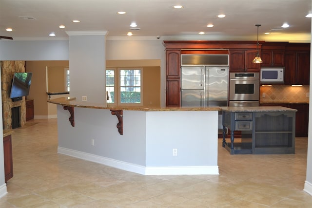 kitchen featuring appliances with stainless steel finishes, decorative light fixtures, light stone counters, and a breakfast bar