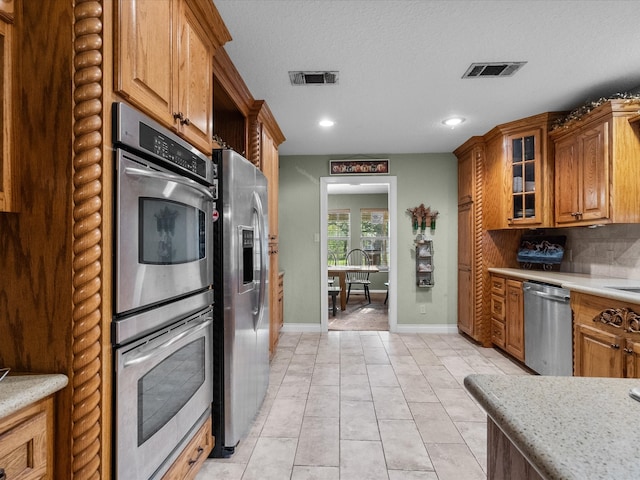 kitchen featuring appliances with stainless steel finishes, backsplash, light stone counters, a textured ceiling, and light tile patterned floors