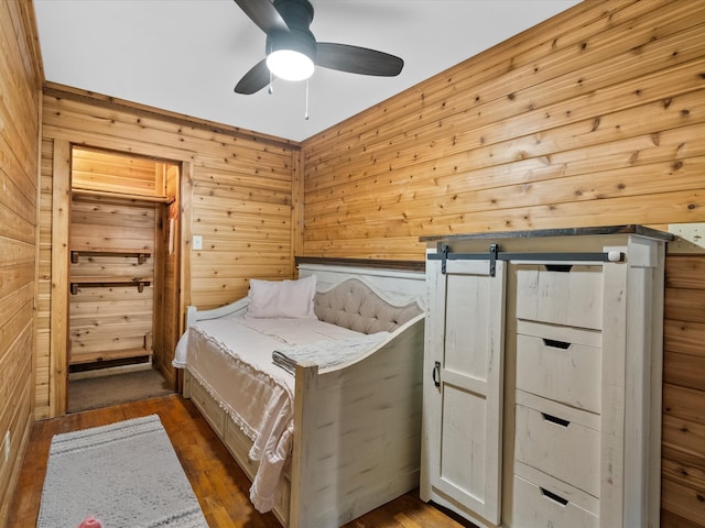 bedroom with a barn door, dark hardwood / wood-style floors, ceiling fan, and wood walls