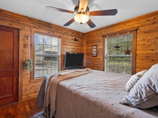 bedroom featuring multiple windows, ceiling fan, dark hardwood / wood-style flooring, and wood walls