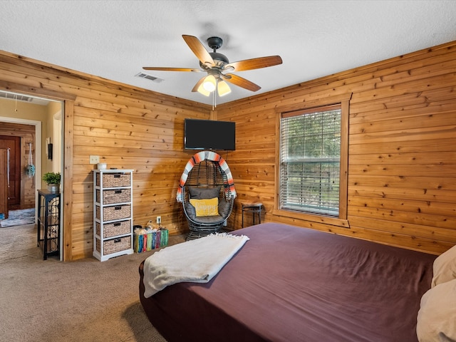 carpeted bedroom with wood walls, ceiling fan, and a textured ceiling