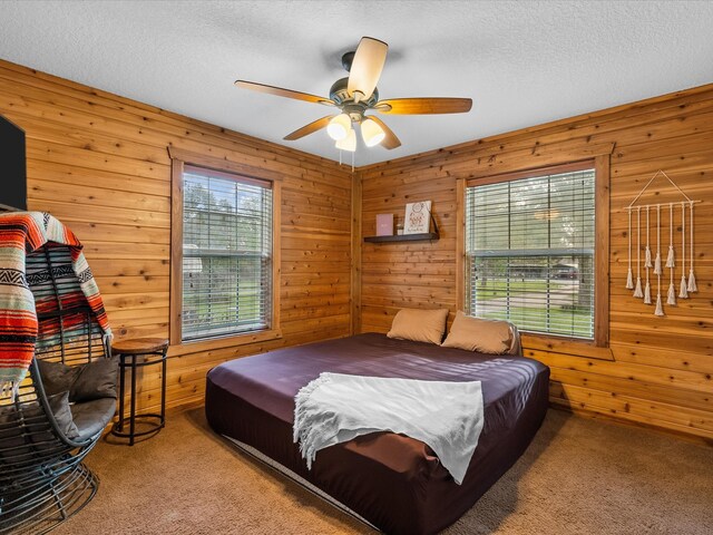 carpeted bedroom featuring a textured ceiling, ceiling fan, and wood walls