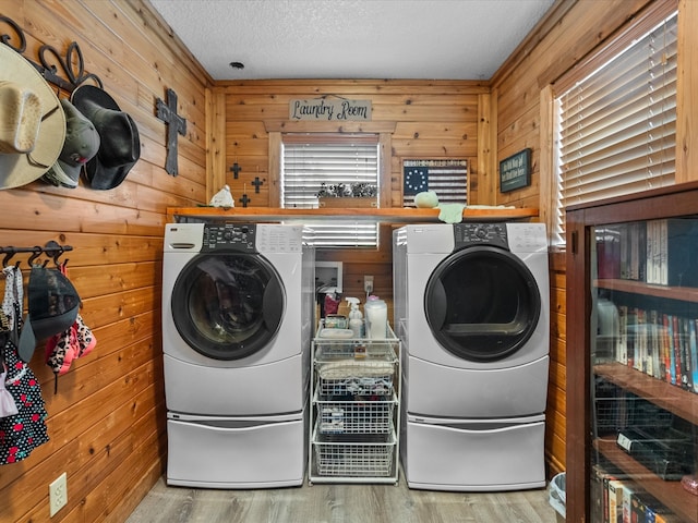 clothes washing area with wooden walls, washer and dryer, and light hardwood / wood-style floors