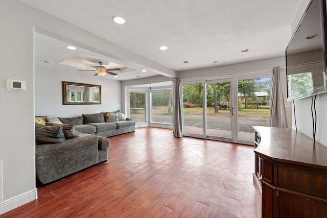 living area with baseboards, a ceiling fan, wood finished floors, a tray ceiling, and recessed lighting