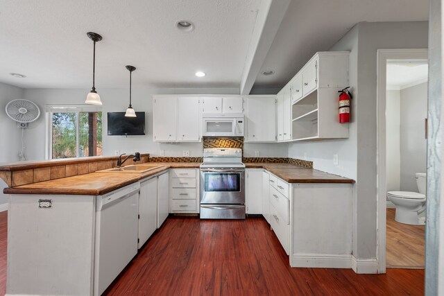 kitchen with a peninsula, white appliances, dark wood finished floors, and a sink