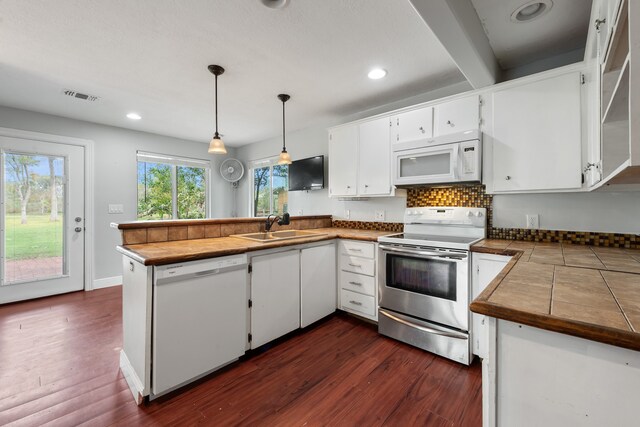 kitchen with a peninsula, white appliances, a sink, visible vents, and dark wood finished floors