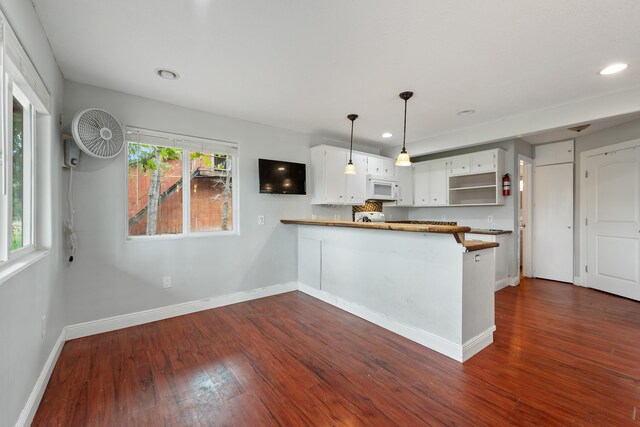 kitchen featuring a peninsula, white microwave, baseboards, and dark wood finished floors