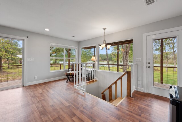 doorway with a notable chandelier, wood finished floors, visible vents, and baseboards