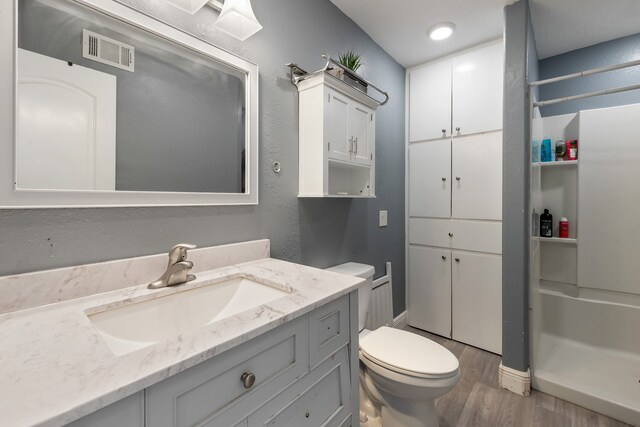 full bathroom with toilet, wood finished floors, vanity, visible vents, and walk in shower