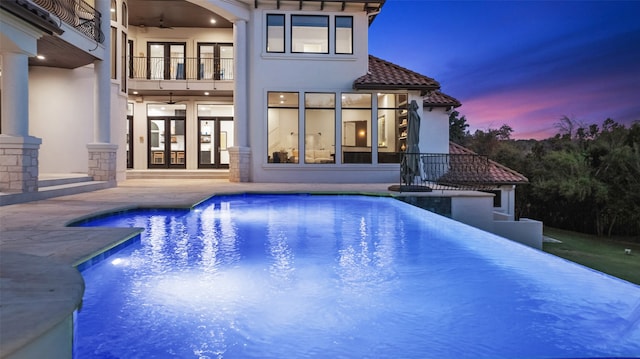 pool at dusk featuring ceiling fan, a patio area, and french doors