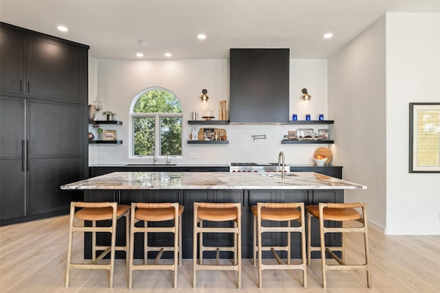 kitchen with extractor fan, light stone counters, light hardwood / wood-style floors, and a large island