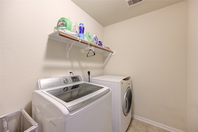 laundry room featuring a textured ceiling, light tile patterned floors, and washer and dryer