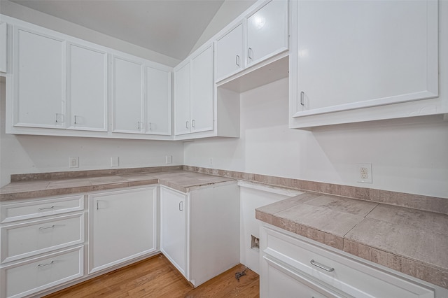 kitchen featuring white cabinets, light wood-type flooring, tile countertops, and vaulted ceiling