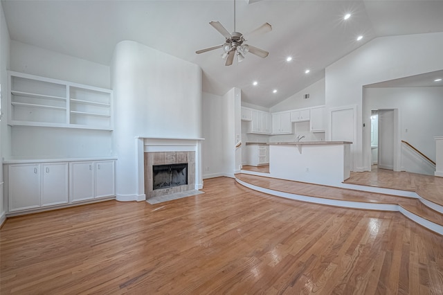 unfurnished living room featuring built in features, a fireplace, high vaulted ceiling, ceiling fan, and light hardwood / wood-style flooring