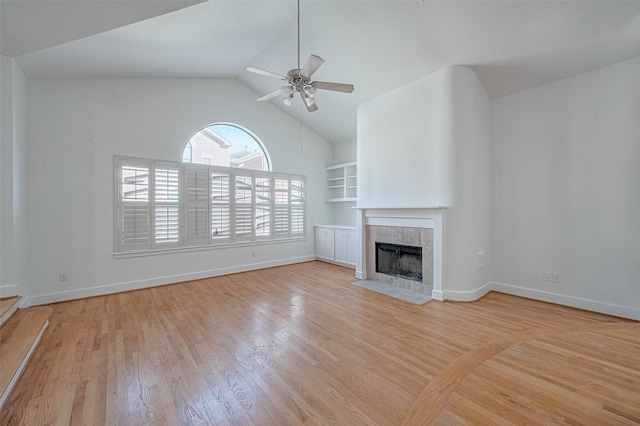 unfurnished living room featuring built in shelves, vaulted ceiling, a tile fireplace, ceiling fan, and light hardwood / wood-style flooring