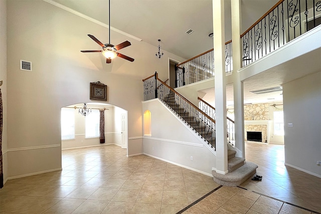 unfurnished living room featuring a high ceiling, ceiling fan, a stone fireplace, and light tile patterned flooring