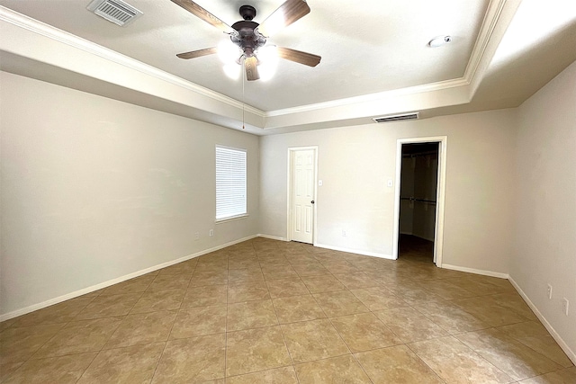 unfurnished bedroom featuring a closet, a walk in closet, crown molding, a tray ceiling, and ceiling fan