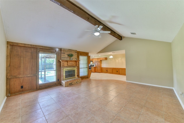 unfurnished living room with light tile patterned flooring, ceiling fan, vaulted ceiling with beams, a brick fireplace, and wooden walls