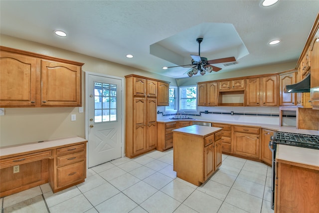 kitchen featuring a center island, sink, stainless steel range with gas cooktop, ceiling fan, and a raised ceiling