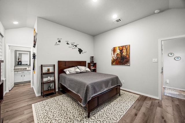 bedroom featuring ensuite bathroom, light hardwood / wood-style flooring, and vaulted ceiling