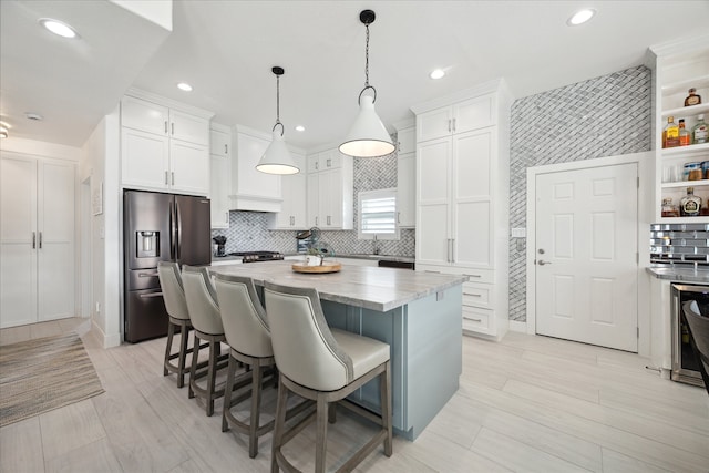 kitchen featuring white cabinetry, light stone counters, stainless steel fridge, decorative light fixtures, and a kitchen island