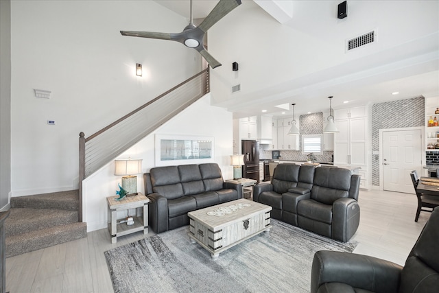 living room with a high ceiling, light wood-type flooring, and ceiling fan