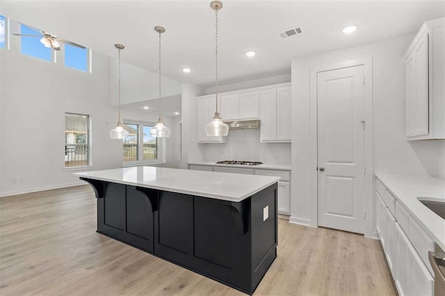 kitchen with white cabinetry, a center island, ceiling fan, stainless steel gas cooktop, and a breakfast bar area