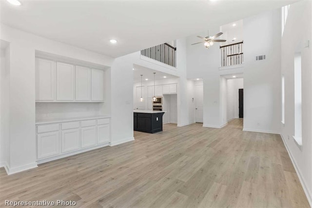 unfurnished living room featuring ceiling fan, light wood-type flooring, and a high ceiling