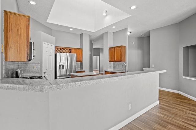 kitchen featuring tasteful backsplash, light wood-type flooring, appliances with stainless steel finishes, and kitchen peninsula