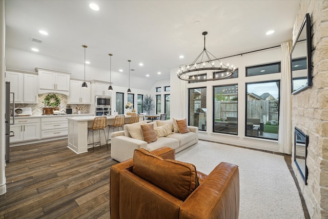 living room with dark wood-type flooring, a fireplace, an inviting chandelier, and lofted ceiling