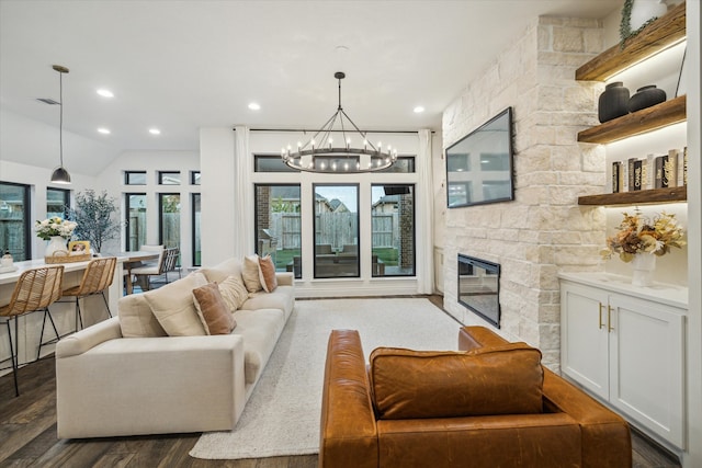 living room with a stone fireplace, vaulted ceiling, a notable chandelier, and dark hardwood / wood-style floors