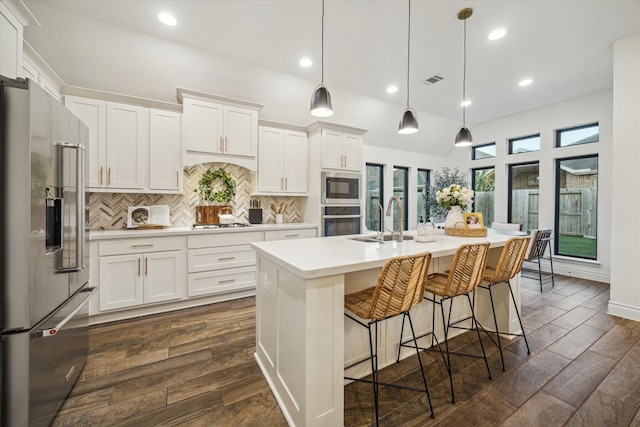 kitchen with hanging light fixtures, an island with sink, dark hardwood / wood-style floors, white cabinetry, and appliances with stainless steel finishes