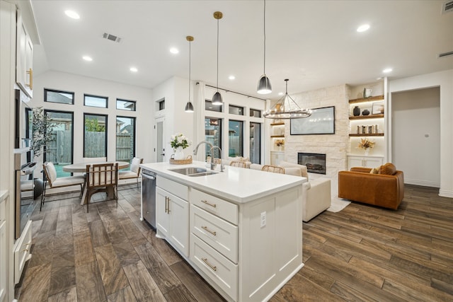 kitchen featuring a center island with sink, sink, white cabinetry, a fireplace, and pendant lighting