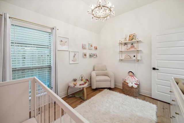 bedroom featuring hardwood / wood-style floors, a crib, a chandelier, and lofted ceiling