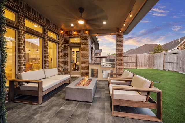 patio terrace at dusk with an outdoor living space with a fire pit, grilling area, a lawn, area for grilling, and ceiling fan