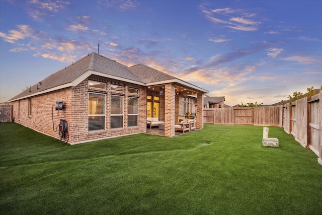 back house at dusk with a lawn and a patio area