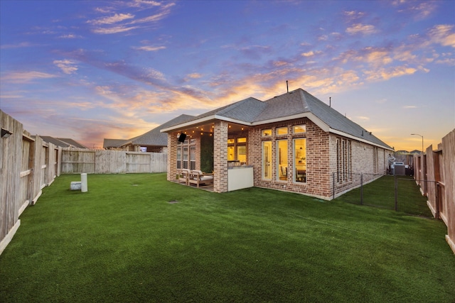 back house at dusk featuring a lawn