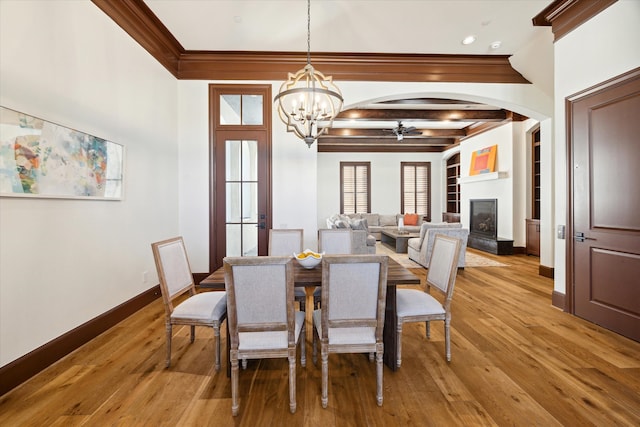 dining space with crown molding, beamed ceiling, ceiling fan with notable chandelier, and light wood-type flooring