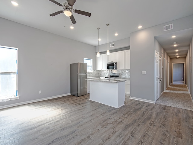 kitchen with white cabinets, stainless steel appliances, pendant lighting, and light hardwood / wood-style flooring