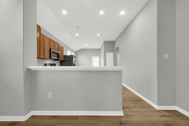 kitchen with kitchen peninsula, lofted ceiling, light wood-type flooring, and appliances with stainless steel finishes