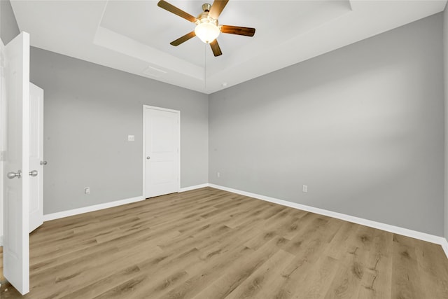 empty room featuring light hardwood / wood-style flooring, ceiling fan, and a raised ceiling