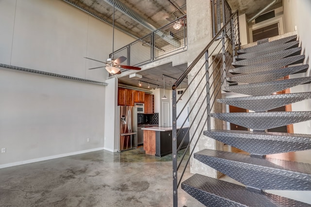 stairway featuring a high ceiling, ceiling fan, and concrete floors