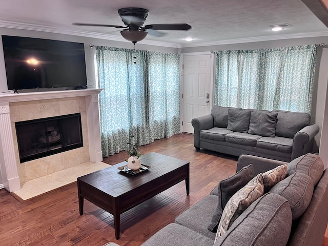 living room featuring a tiled fireplace, wood-type flooring, ceiling fan, and crown molding