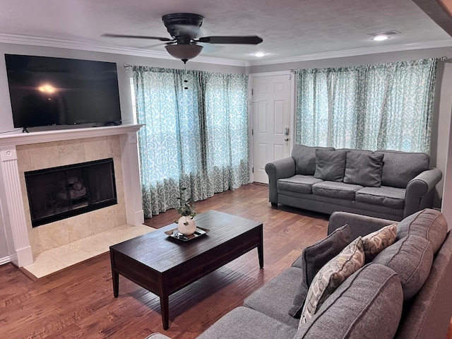 living room featuring hardwood / wood-style floors, ceiling fan, crown molding, and a tiled fireplace