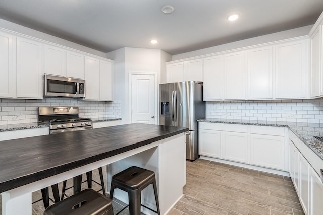 kitchen featuring white cabinetry, appliances with stainless steel finishes, and dark stone counters