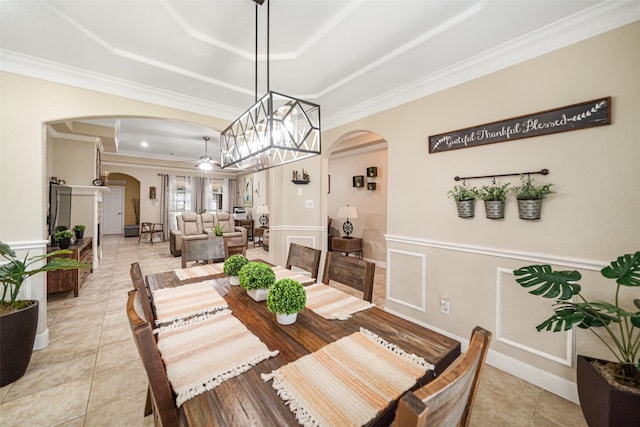 dining room with ceiling fan with notable chandelier, a raised ceiling, light tile patterned floors, and crown molding