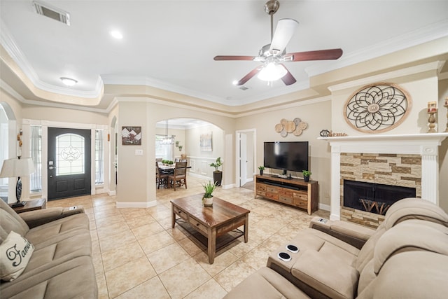 living room with ceiling fan, a stone fireplace, light tile patterned floors, and crown molding